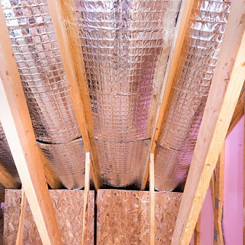 The interior view of a roof's gable.  The beams of the home are exposed and there is aluminum insulation showing.